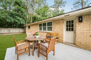 Ein Haus mit einer Terrasse, auf der sich ein runder Holztisch und Stühle, ein Blumentopf und eine Ziegelaußenwand befinden.