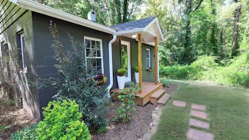 Une petite maison dotée d’un porche, entourée d’un jardin bien entretenu et d’arbres.