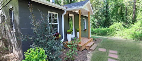 A small house with a porch, surrounded by a well-maintained garden and trees.