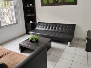 A modern living room with a black sofa, a small coffee table with plants, and a window with a view of trees. - Casa pame! (CHELEM)