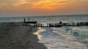 A beach with a wooden pier extending into the sea, waves gently lapping at the shore, and a sunset in the background. - Peaceful 1-bedroom house in charming Chelem perfect for relaxing stays (CHELEM)
