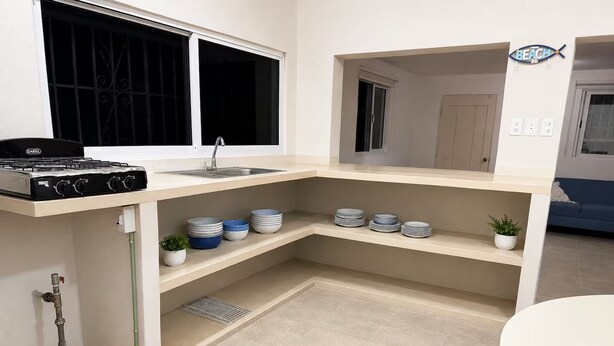 A modern kitchen with a gas stove, sink, and a corner shelf with plates. - Peaceful 1-bedroom house in charming Chelem perfect for relaxing stays (CHELEM)