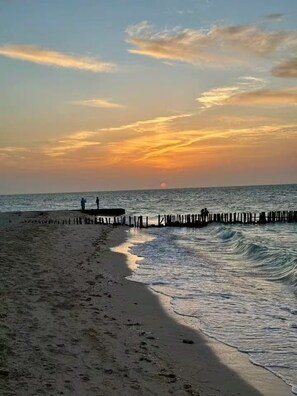 A beach with a wooden pier extending into the sea, waves gently lapping at the shore, and a sunset in the background. - Marvelous 1-bedroom house in charming Chelem perfect for relaxing getaway (CHELEM)