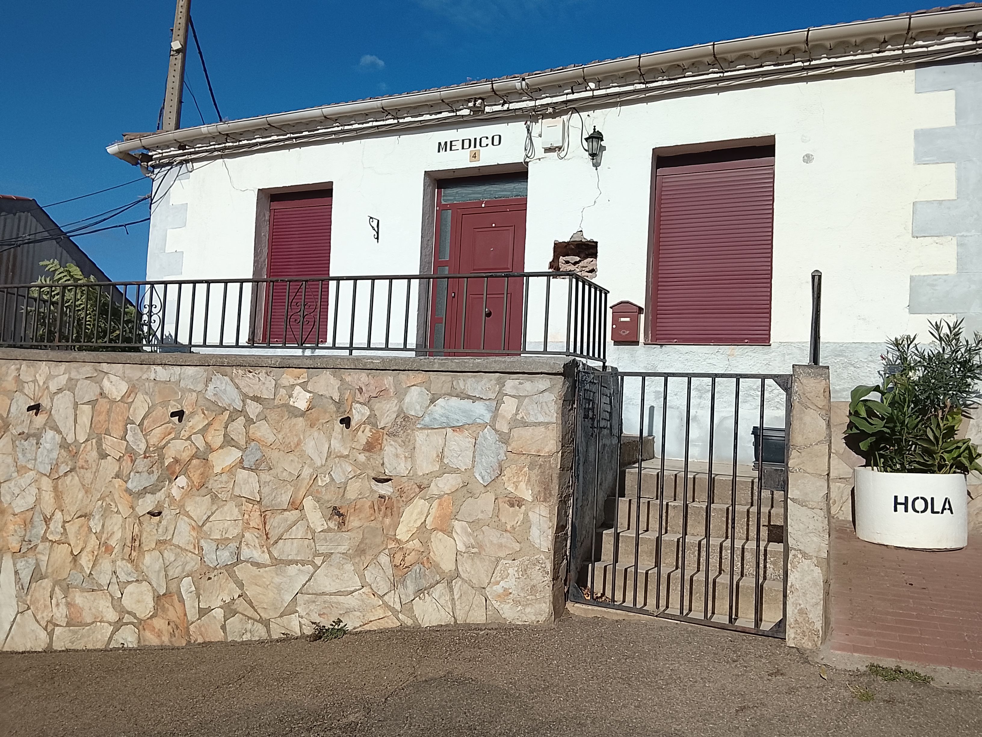 A building with a stone wall, a metal gate, and a red door labeled 'MEDICO'.