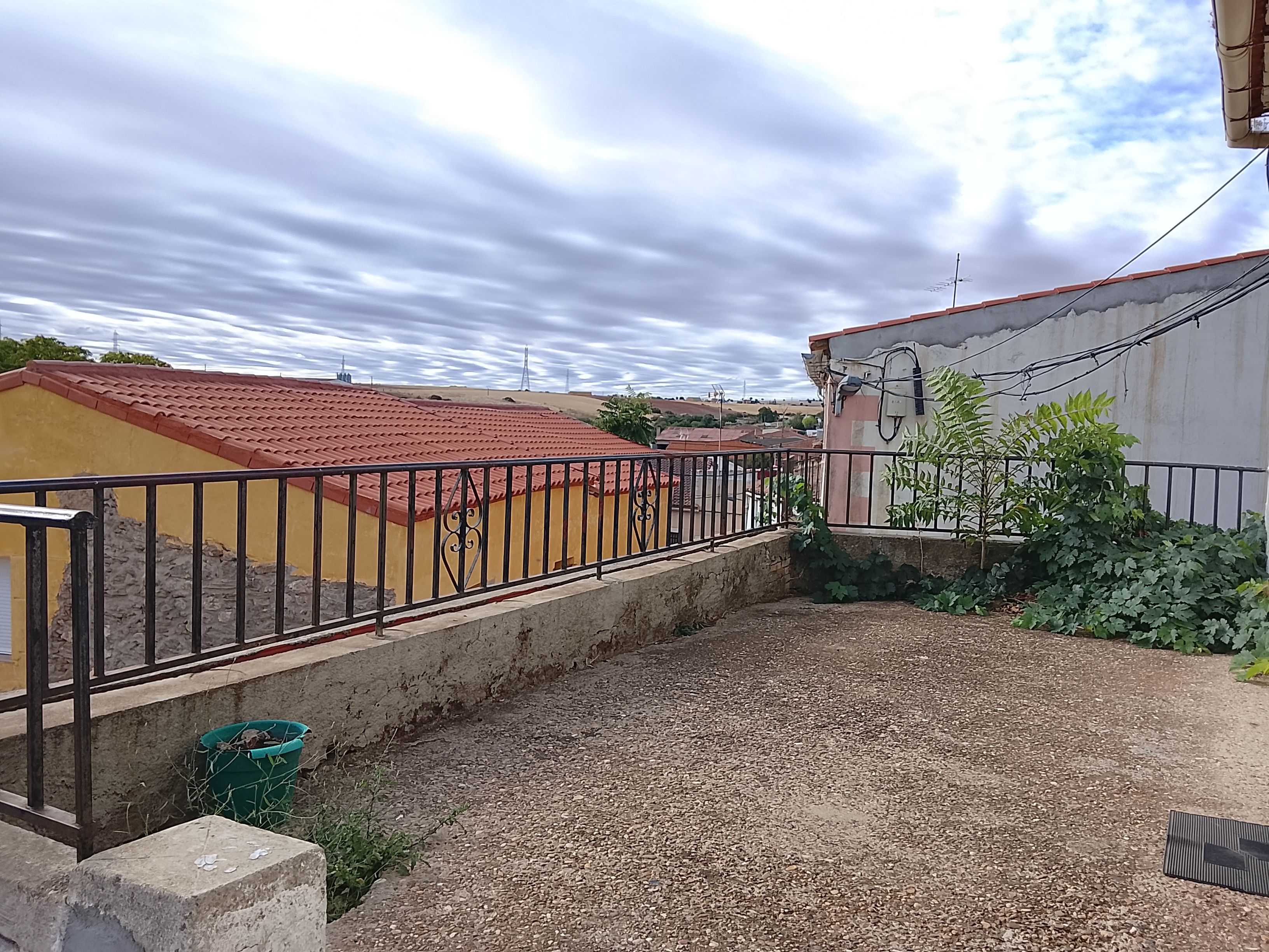 A courtyard with a gravel ground, a metal fence, and a building with a red roof.