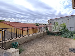 A courtyard with a gravel ground, a metal fence, and a building with a red roof.