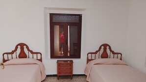 Une pièce avec deux lits en bois, une petite commode en bois et une fenêtre avec des stores.