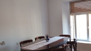 Un coin repas comprenant une table rectangulaire, six chaises, une carafe et une fenêtre avec des stores.