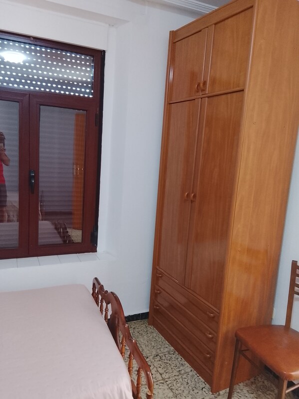 A bedroom with a bed, a wardrobe, a window, and a chair.