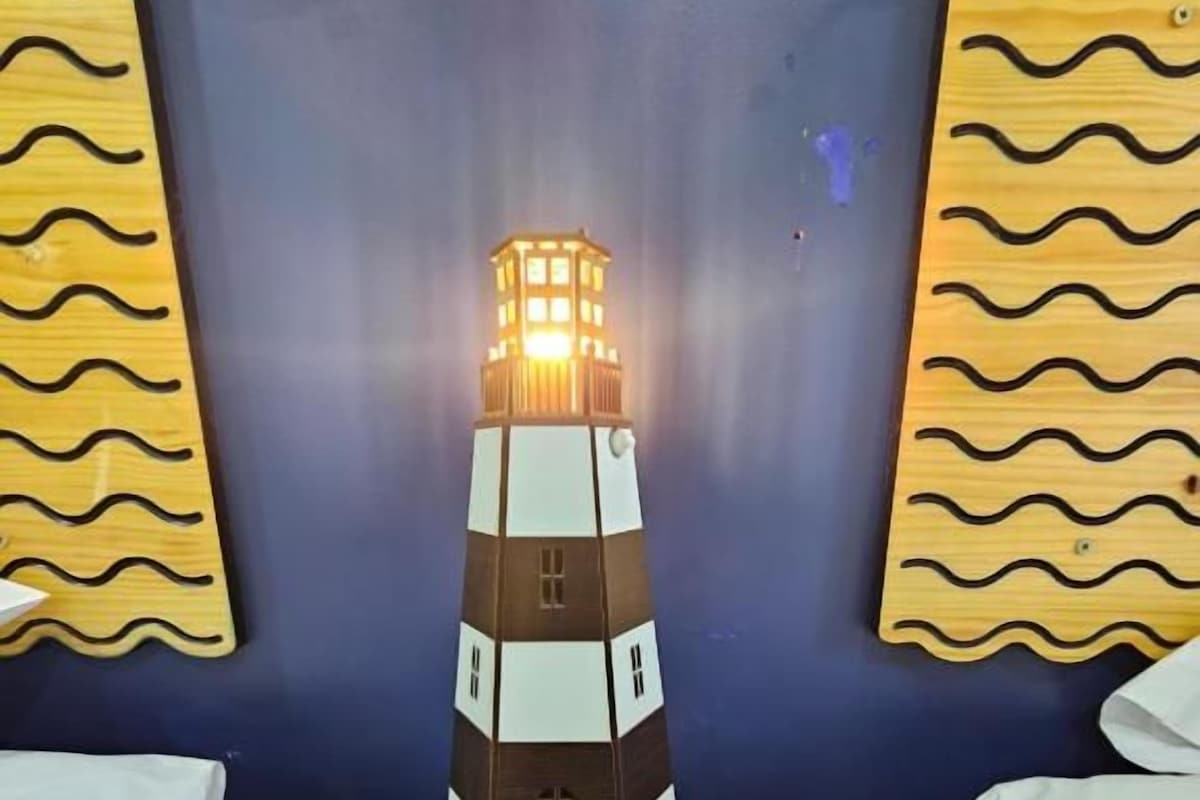 A model lighthouse on a wooden nightstand in a room with a dark blue wall.