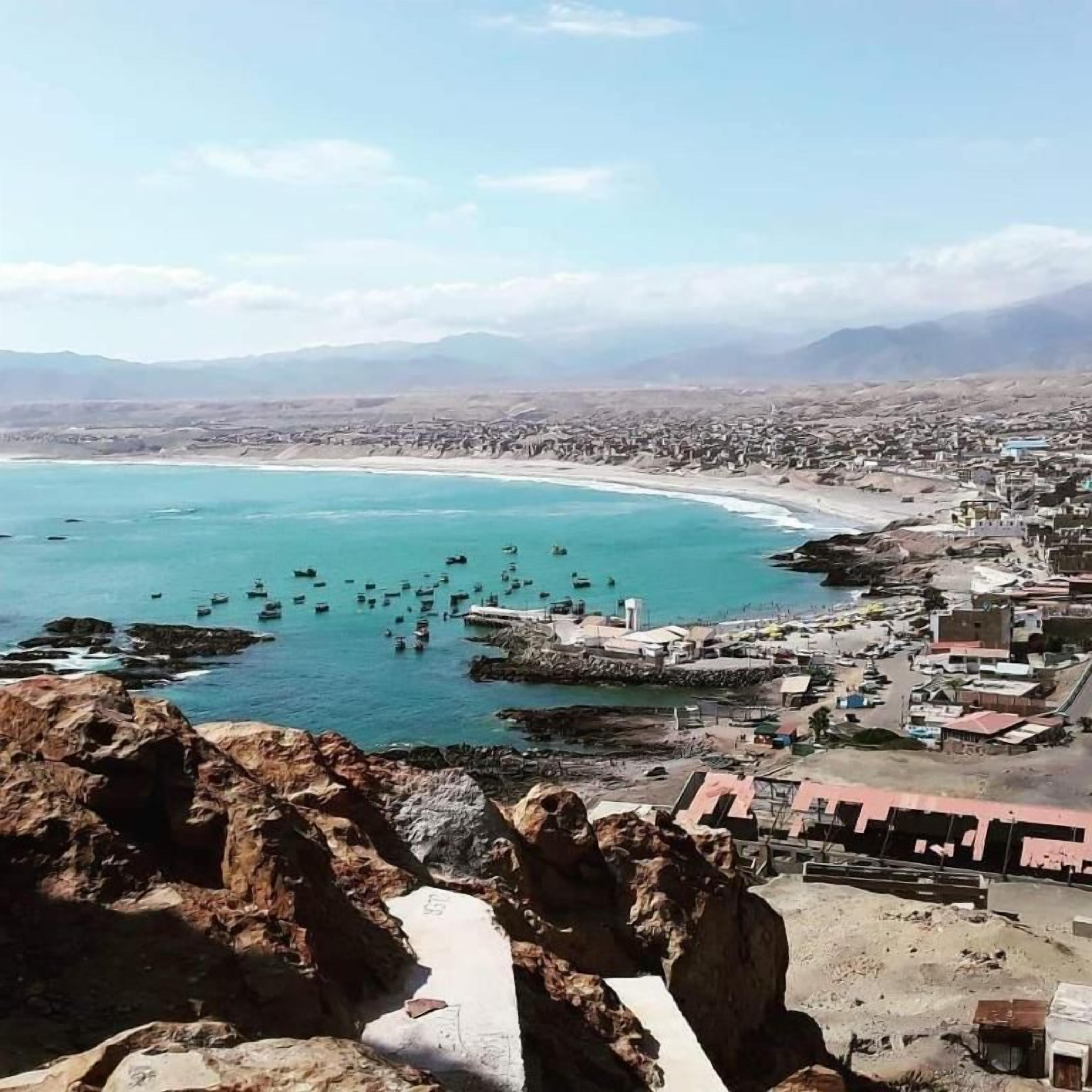 Un pueblo costero con un litoral rocoso, barcos en el agua y edificios a lo largo de la playa.