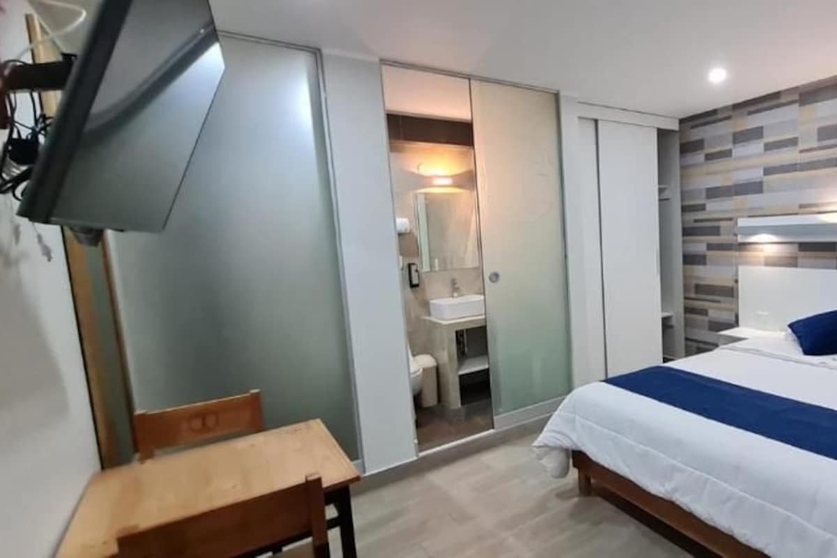 A modern bedroom with a bed, bedside tables, a desk, and a TV.