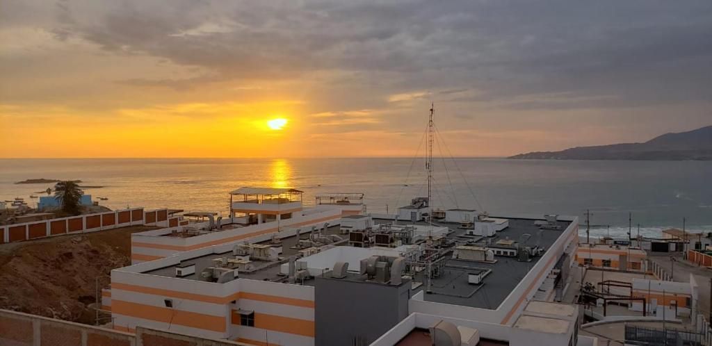 A rooftop with multiple buildings, a clear sky, and a sunset over the sea.