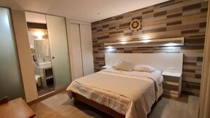 A hotel room with a bed, a wardrobe, a mirror, and a wall-mounted clock.