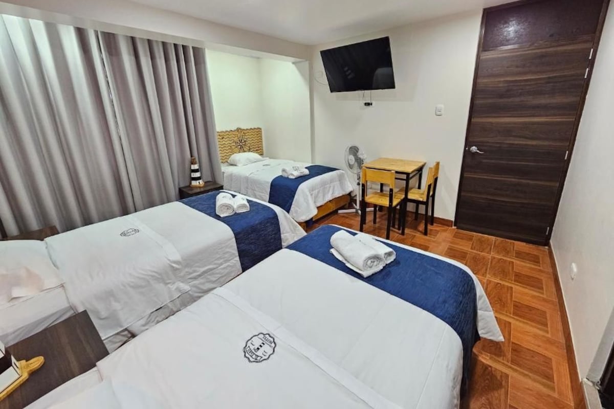 A hotel room with two beds, a desk, a chair, a television, and a door.