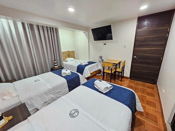 Habitación de hotel con dos camas, un escritorio, una silla, un televisor y una puerta.