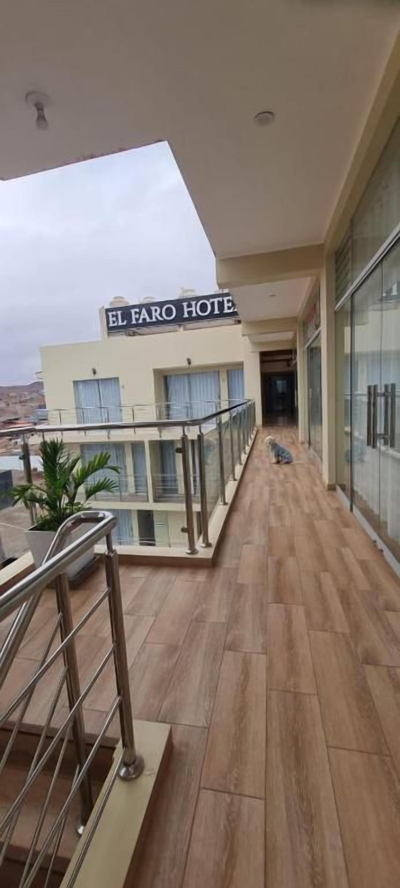 Un pasillo de hotel con barandilla de vidrio, un letrero que dice 'EL FARO HOTEL' y vista del paisaje urbano.