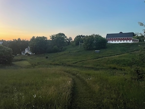 A rural landscape with a white building, a red barn, and a path leading through the field.