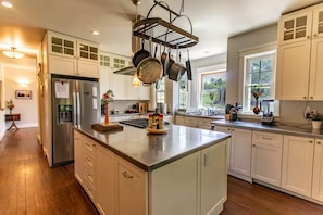 A modern kitchen with white cabinetry, a central island, and a hanging pot rack.