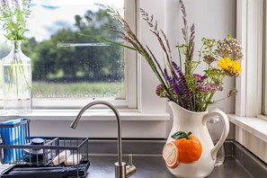 A kitchen sink with a faucet, a dish rack, and a vase with flowers on the window sill.