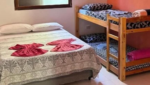 Une chambre comprenant un lit, un lit superposé, une fenêtre avec des stores et un climatiseur fixé au mur.
