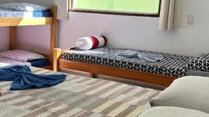 Une chambre de dortoir avec des lits superposés, une fenêtre avec des rideaux et un lit recouvert d’une couverture à motifs.