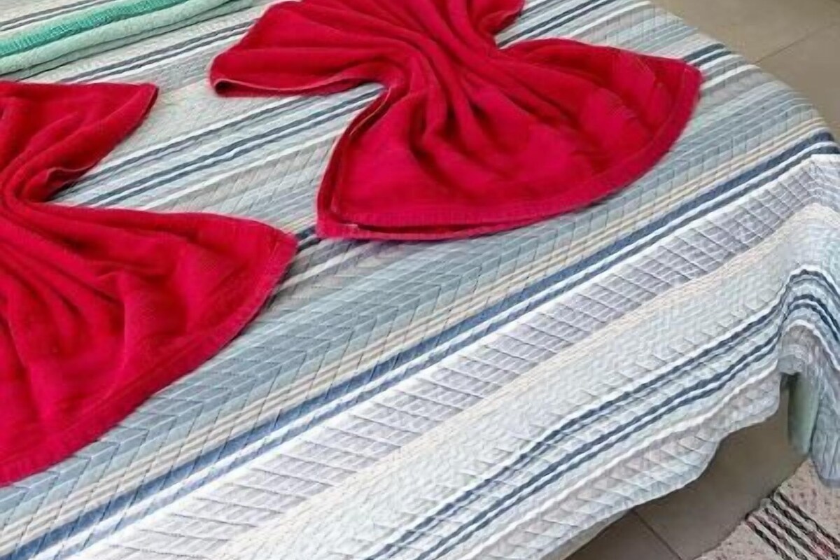 Una cama con una colcha a rayas y dos toallas rojas encima.
