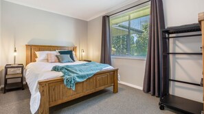 Ein Schlafzimmer mit einem hölzernen Bett, einem Nachttisch, einer Lampe, einem Fenster mit Jalousien und einem Kleiderschrank.