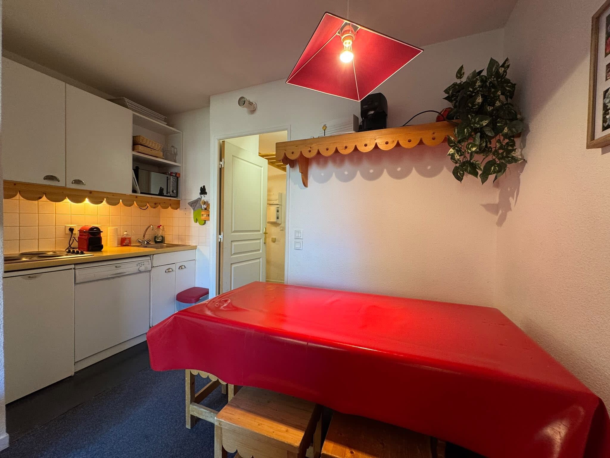A compact kitchen with white cabinets, a red table, and a hanging light fixture.