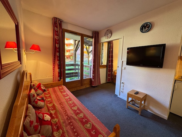 Ein Schlafzimmer mit Bett, Fernseher, einem kleinen Tisch und einer Glastür, die zu einem Außenbereich führt.