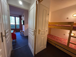 Ein Zimmer mit einem Etagenbett, einer Tür zu einem anderen Raum und einem kleinen Tisch mit Stuhl.