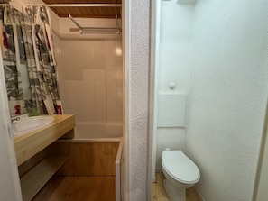 Ein kleines Badezimmer mit einem Holzkosmetikschrank, einer weißen Toilette und einer Duschkabine.