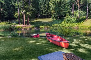 A serene lakeside setting with a red canoe, a picnic table, and a row of hanging light bulbs. - 7BR Family Retreat + Private Pond+ Outdoor Kitchen (Oregon City)