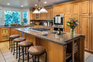 A kitchen with wooden cabinets, a large island with stools, a stove, and a vase of flowers. - 7BR Family Retreat + Private Pond+ Outdoor Kitchen (Oregon City)