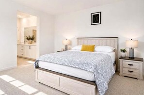 A bedroom with a bed, bedside tables, a nightstand, a mirror, and a wall-mounted picture.