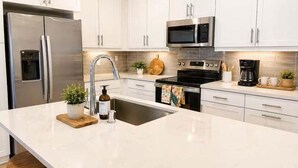 A modern kitchen with white cabinets, stainless steel appliances, and a large island with a sink. - Fully Furnished 3BR and 3BA Retreat with Views (Eastvale)