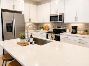A modern kitchen with white cabinets, stainless steel appliances, and a large island with a sink.