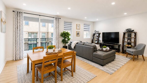 A modern living room with a dining table, grey sofa, and a flat-screen TV.