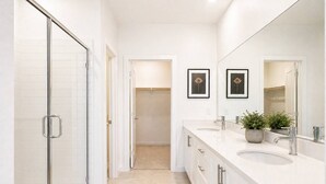 A modern bathroom with a glass shower enclosure, a walk-in closet, and a vanity with two sinks and a large mirror. - Fully Furnished 3BR and 3BA Retreat with Views (Eastvale)