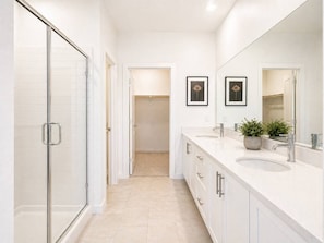 A modern bathroom with a glass shower enclosure, a walk-in closet, and a vanity with two sinks and a large mirror.