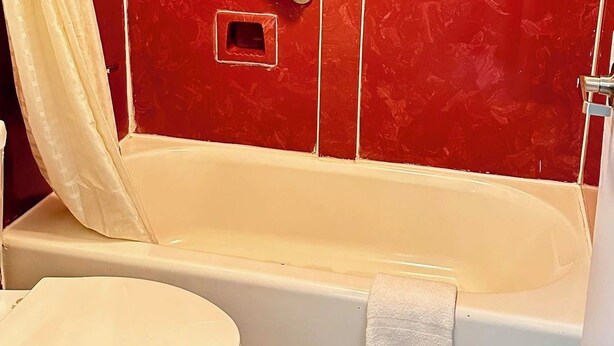 Un baño con pared de azulejos rojos, inodoro blanco y bañera con toalla.