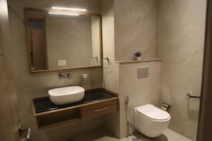 Un baño moderno con un espejo grande, un lavabo sobre encimera, un inodoro y una ducha.