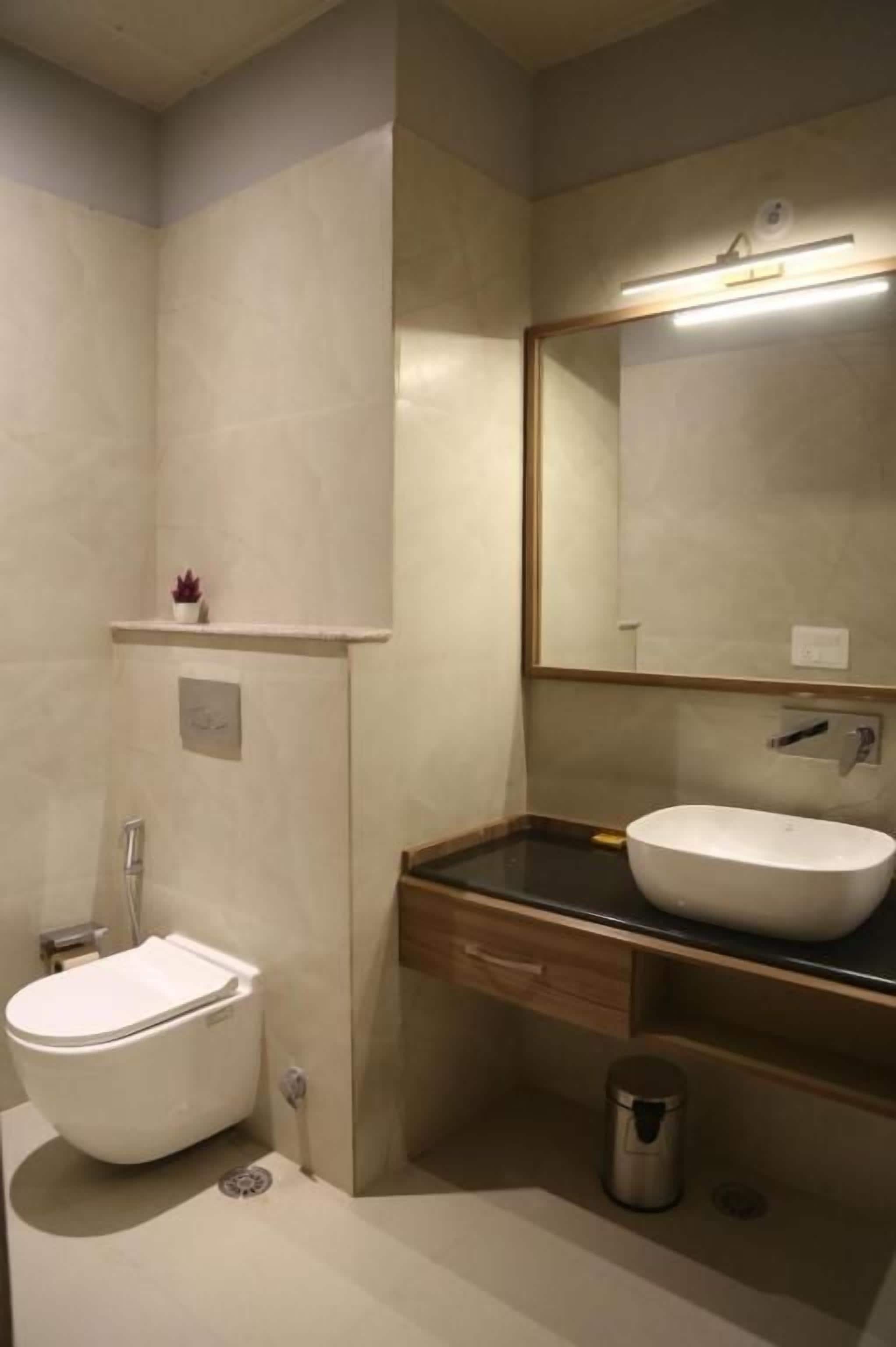 Ein Badezimmer mit Toilette, Waschbecken, Spiegel und einem kleinen Regal mit einer Pflanze.