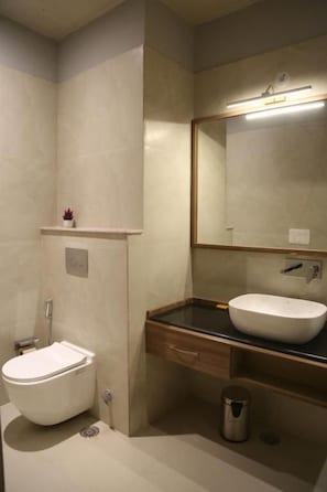 Ein Badezimmer mit Toilette, Waschbecken, Spiegel und einem kleinen Regal mit einer Pflanze.
