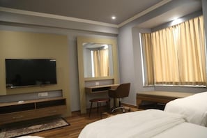 Habitación de hotel con cama, escritorio, silla, televisor y una ventana grande con cortinas.