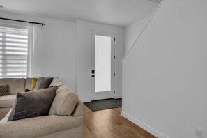 Un salon moderne avec un canapé, une porte et une fenêtre équipée de stores.