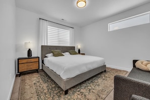 Une chambre à coucher avec un lit, des tables de chevet, une fenêtre avec des stores, un tapis et une chaise.