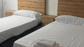 Quarto de hotel com duas camas, cada uma com cabeceira de madeira, roupa de cama branca e toalha dobrada sobre a cama.