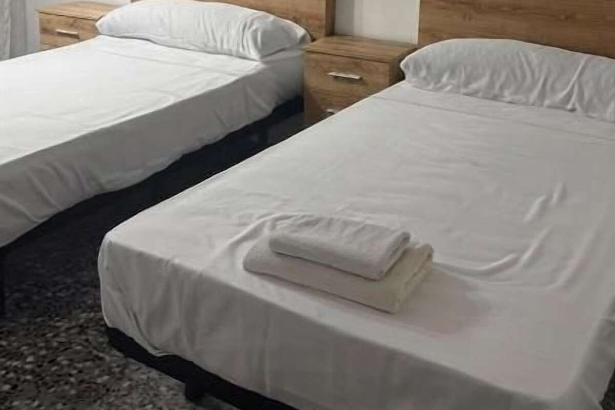 Et hotelværelse med to senge, hver med et træhovedgærde, hvidt sengetøj og et pænt foldet håndklæde på sengen.