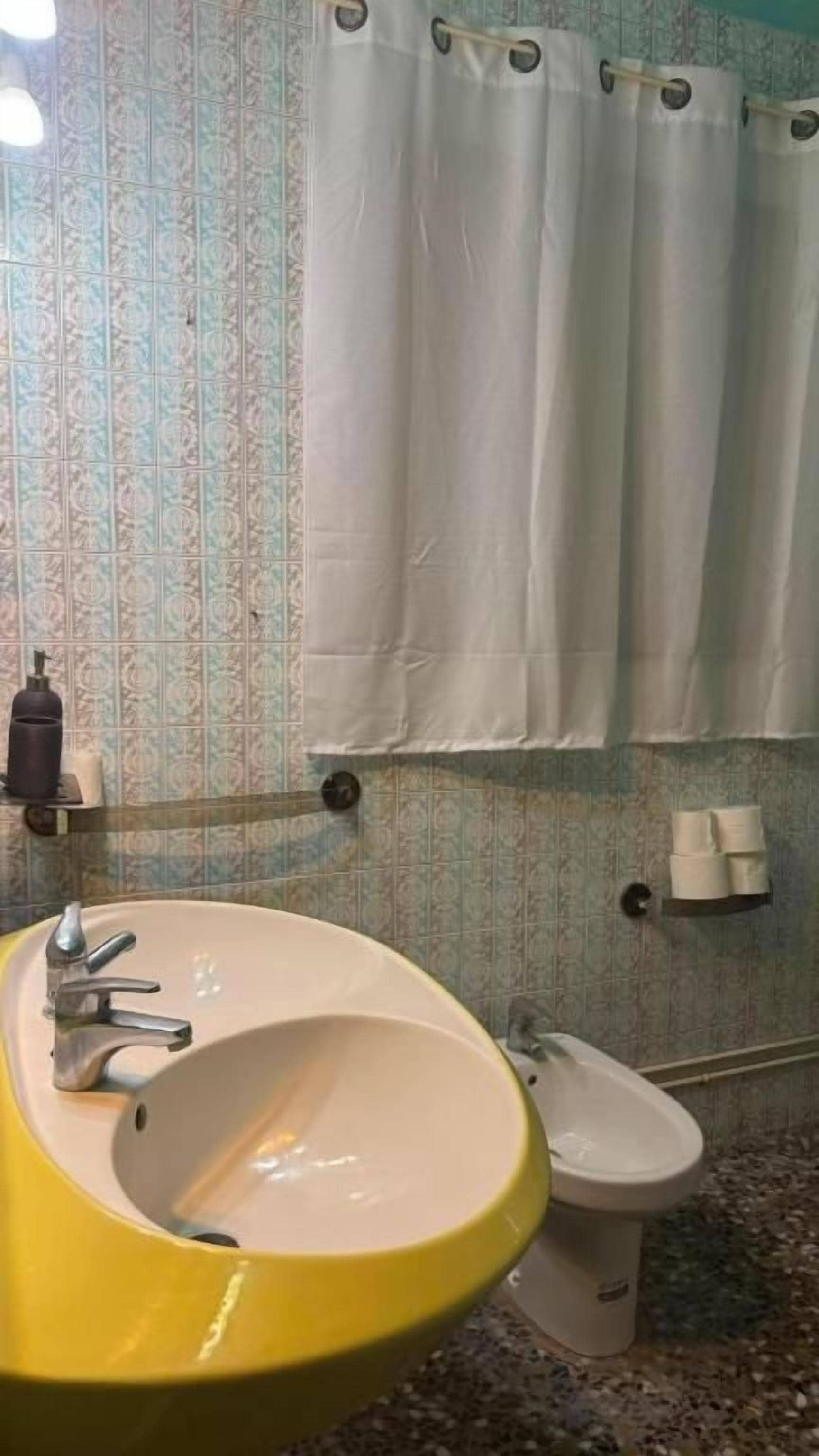 Un baño con lavamanos amarillo, inodoro blanco y cortina de ducha.